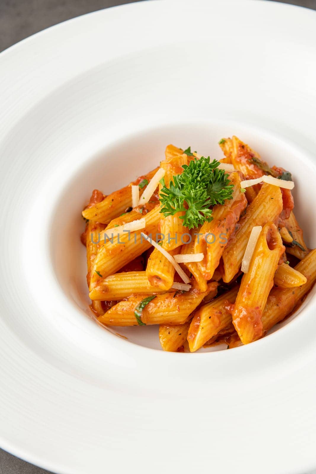 Penne pasta in tomato sauce, tomatoes decorated with parsley on a wooden background