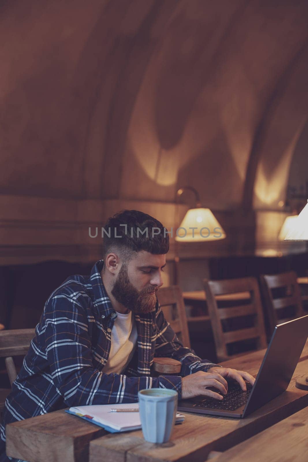 Young professional surfing the Internet on his laptop with cup of coffee on table at coffee shop or home office, working from cafe concept