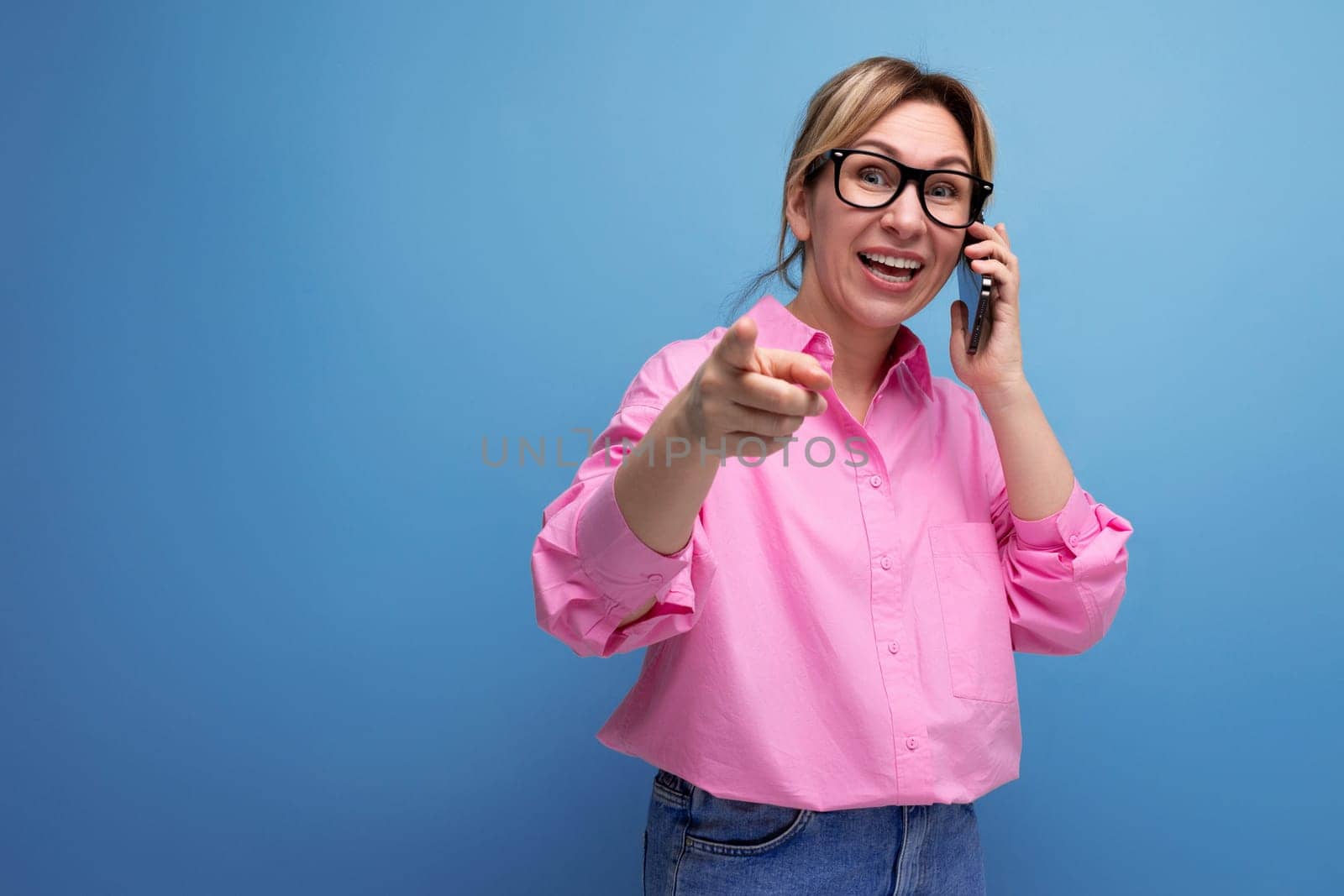 young surprised caucasian blonde secretary woman with ponytail hairstyle, glasses and pink shirt chatting on the phone by TRMK