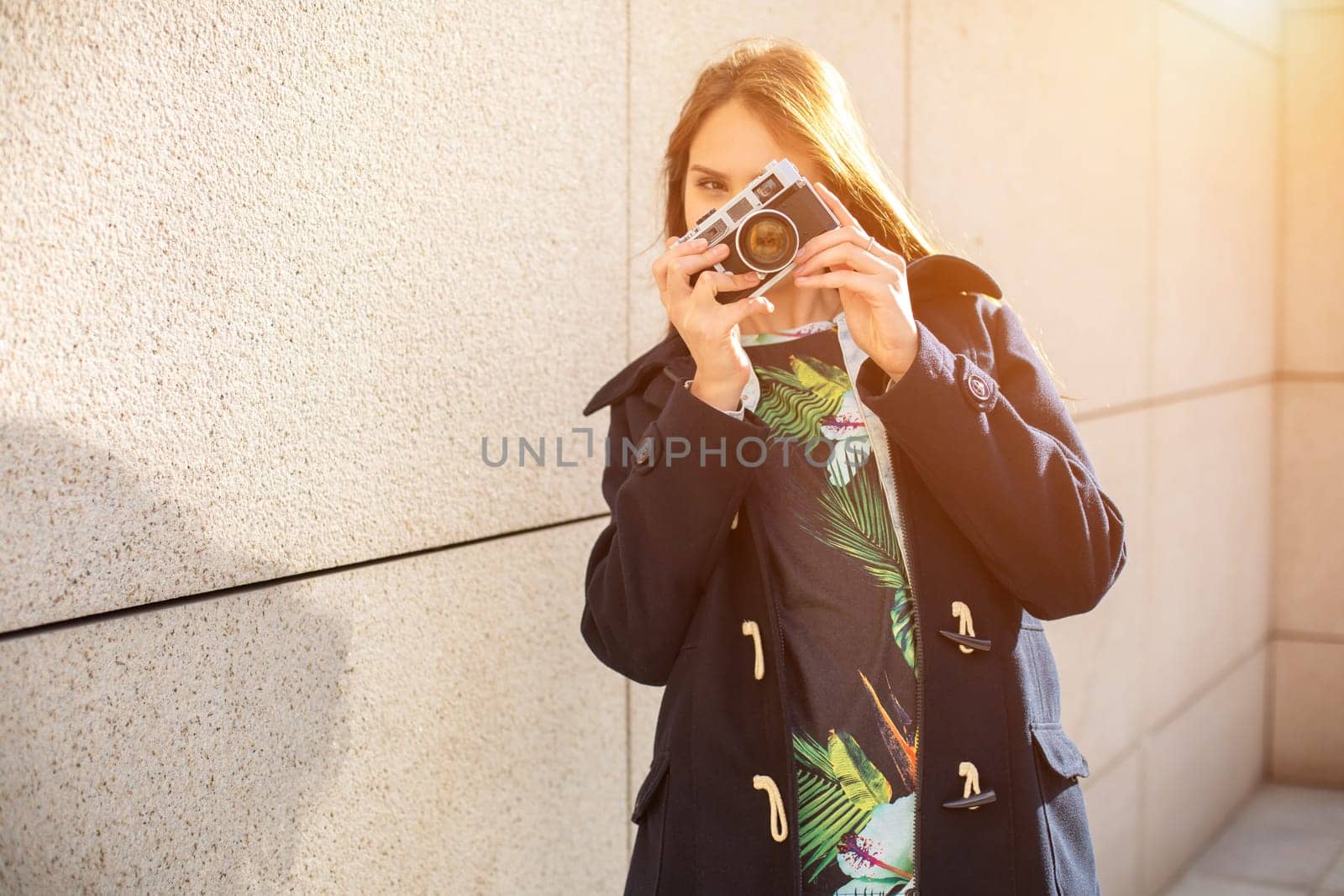 Happy hipster girl making photo with retro camera on city street. Sun flare by nazarovsergey