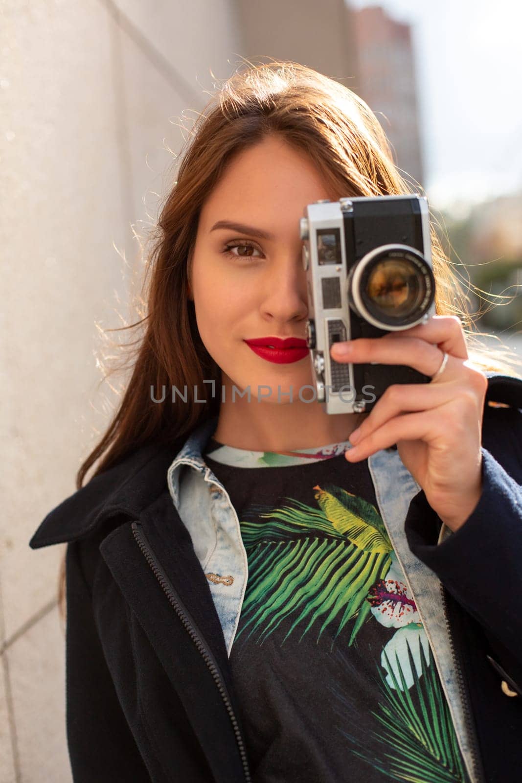 Happy hipster girl making photo with retro camera on city street by nazarovsergey