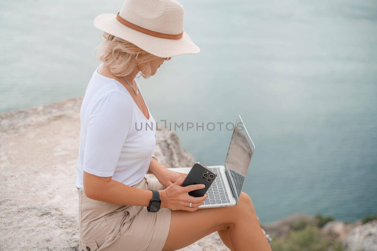 Freelance women sea working on the computer. Good looking middle aged woman typing on a laptop keyboard outdoors with a beautiful sea view. The concept of remote work