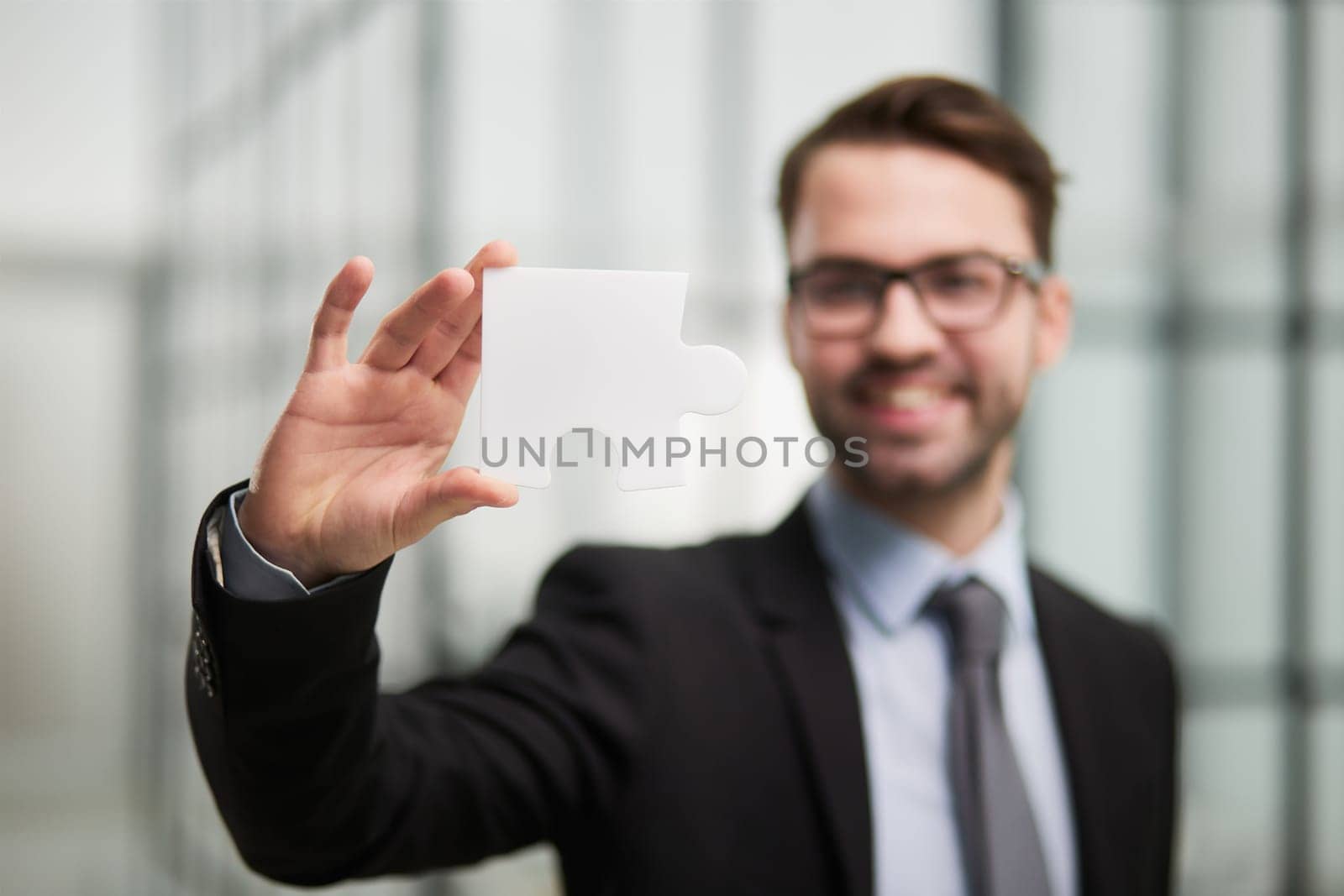 Portrait of an optimistic businessman holding puzzle pieces, solving problems, looking at the camera, wearing a black suit.