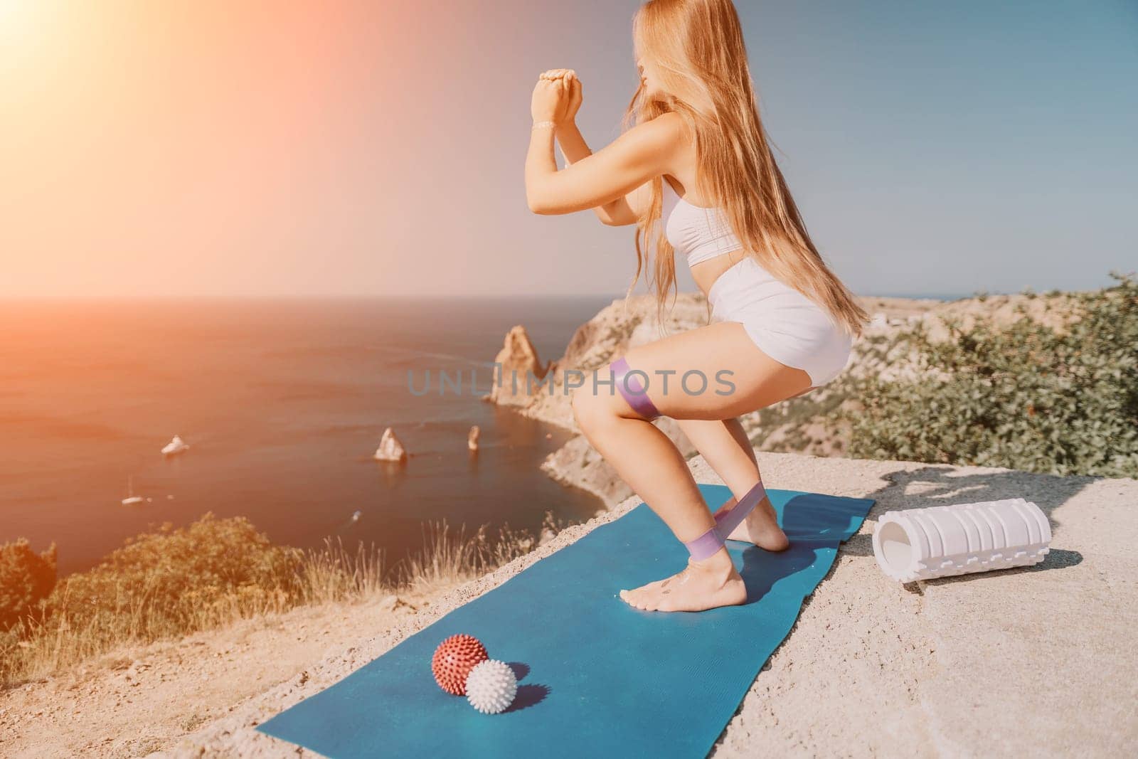 Woman sea pilates. Sporty happy middle aged woman practicing fitness on yoga mat using rubber tape, massage balls, and rollers near sea, smiling active female outside, enjoying healthy lifestyle by panophotograph