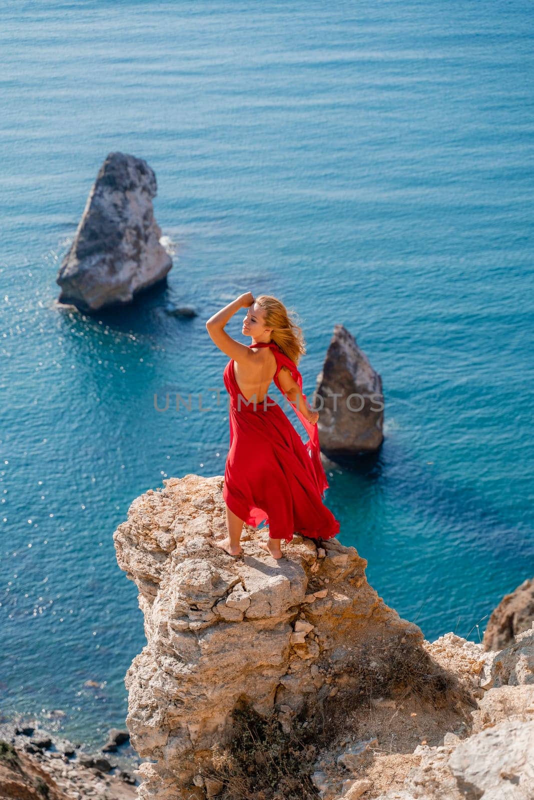 A woman in a red flying dress fluttering in the wind, against the backdrop of the sea