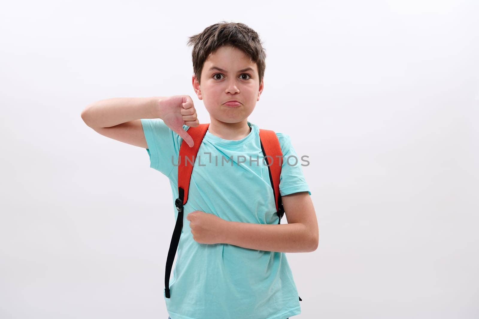 Preteen schoolboy thumbs down at camera, feels negative emotions, aggressive attitude, suffering from act of bullying at school, education difficulties, psychological problems, isolated background