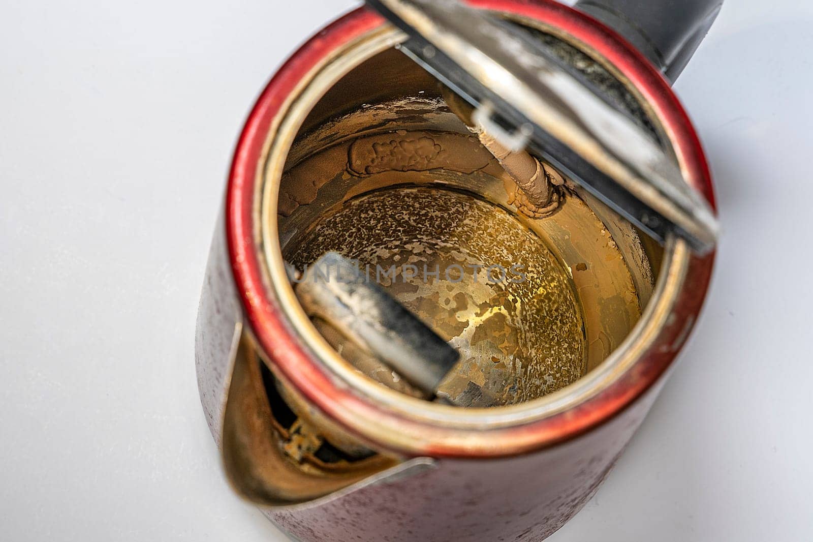 An old electric kettle with traces of scale and limescale on the walls and bottom. What happens to unfiltered water during boiling. Calcium-magnesium formations and deposits on the heating element of the kettle.