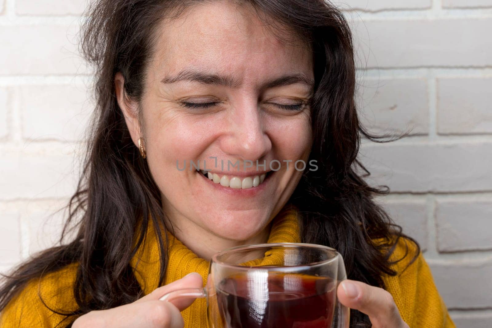 a pretty Caucasian middle-aged woman laughs while spending time with friends or family. enjoys tea while relaxing. glass transparent mug with delicious aromatic tea. Enjoying the moment, Mental health and positive emotions