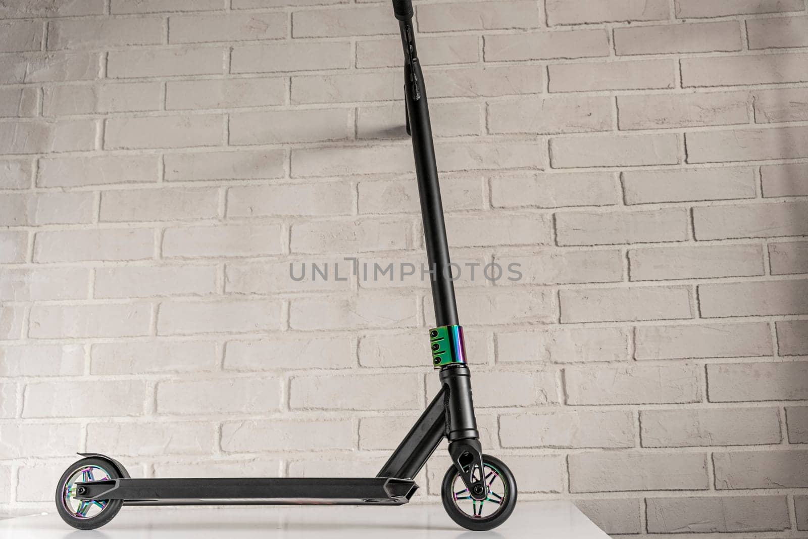 Side view of a stunt scooter with rainbow-colored wheels against a light brick wall. equipment for extreme skating in a skatepark and on a ramp. Details of the scooter. Repair, rental and sale of scooters