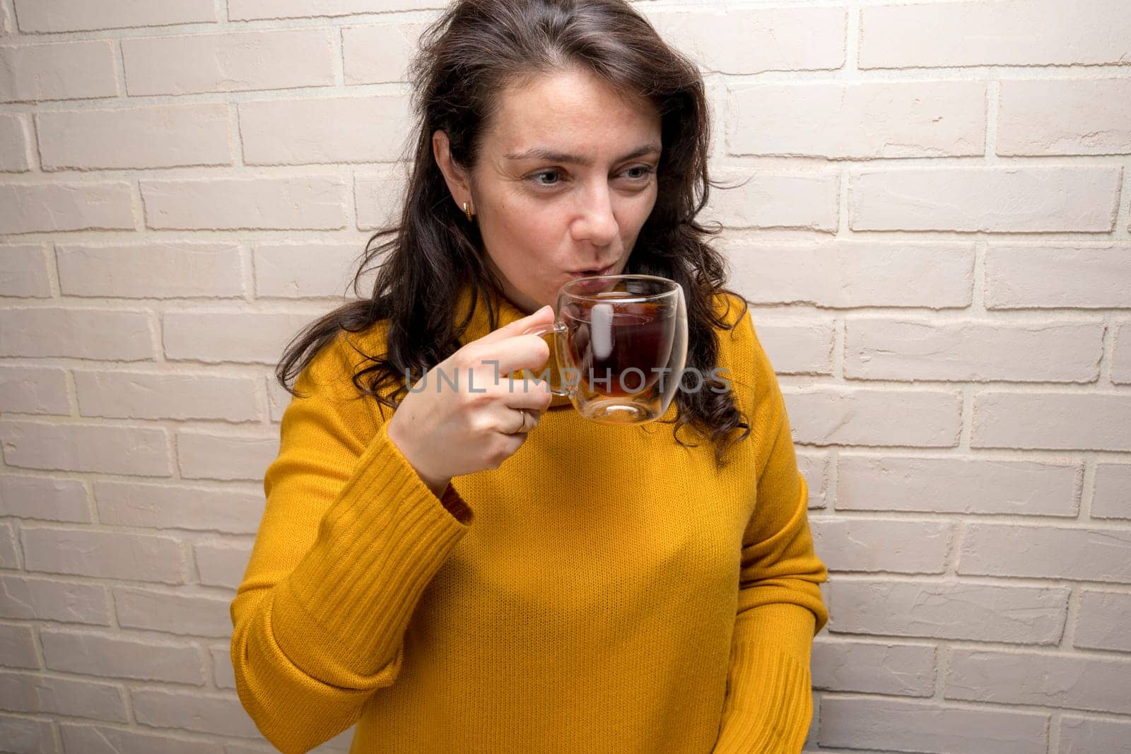 a pretty Caucasian middle-aged woman laughs while spending time with friends or family. enjoys tea while relaxing. glass transparent mug with delicious aromatic tea. Enjoying the moment, Mental health and positive emotions