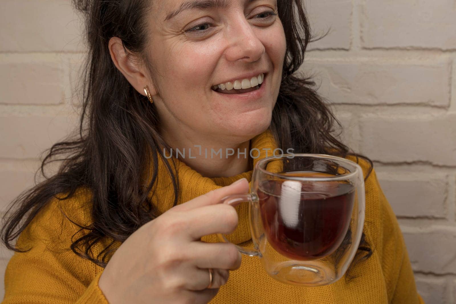 a pretty Caucasian middle-aged woman laughs while spending time with friends or family. enjoys tea while relaxing. glass transparent mug with delicious aromatic tea. Enjoying the moment, Mental health and positive emotions