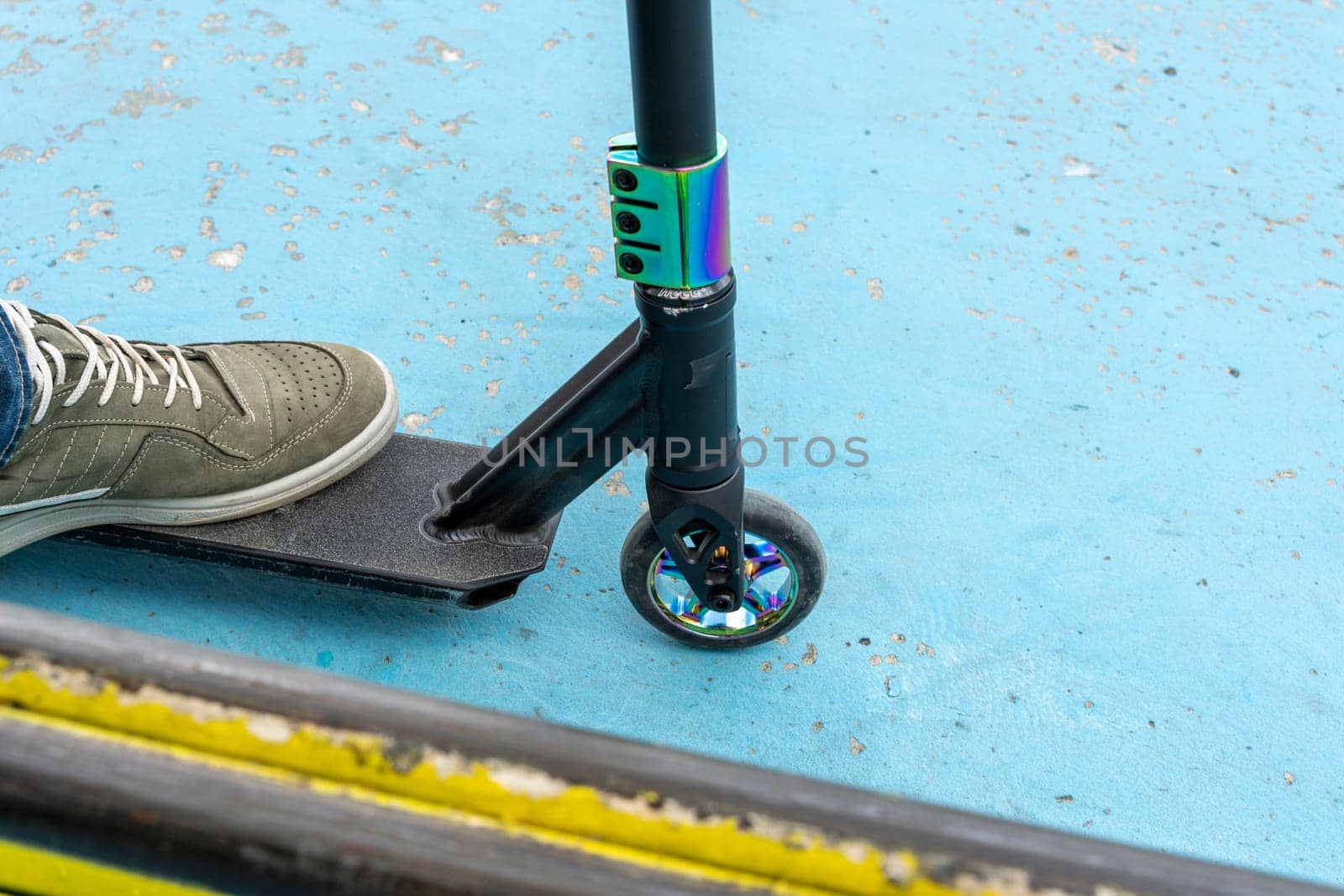 Rider boy legs close up in sneakers on stunt scooter on the skate park ramp. A boy on a scooter in a skate park performs jumps and tricks. extreme city sports outdoor Extreme jumping on a scooter. The concept of a healthy lifestyle. sports leisure