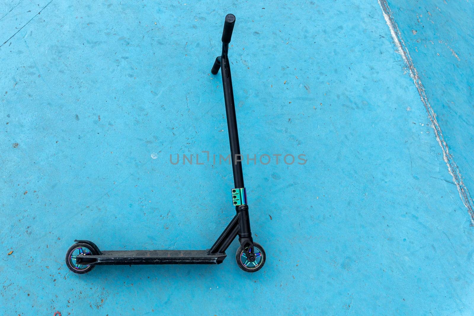 a stunt scooter, a modern extreme stunt scooter in a skate park lies on a concrete path. the scratched scooter lies after falling to the ground. The concept of a healthy lifestyle and sports leisure