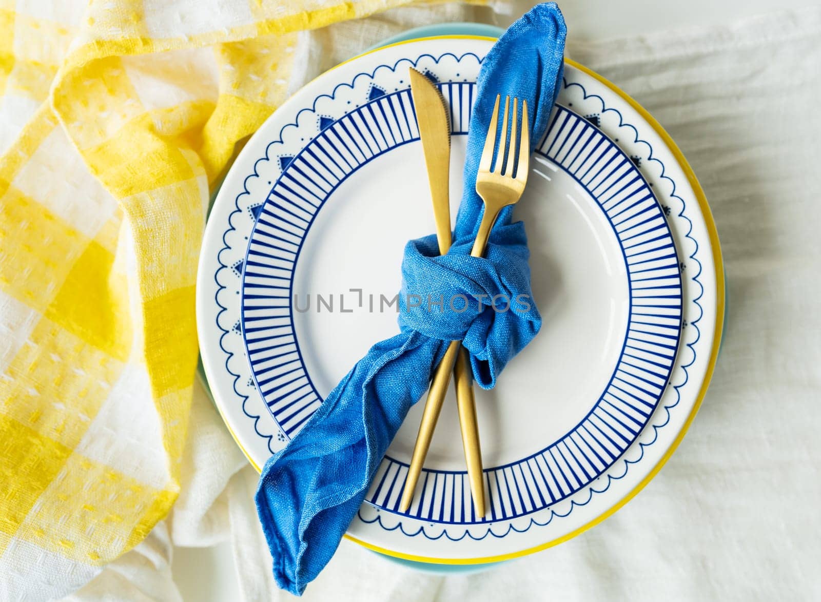 Serving design. Gold cutlery is tied with a blue napkin, on which the plates are on a yellow linen napkin. Minimalistic design, rustic