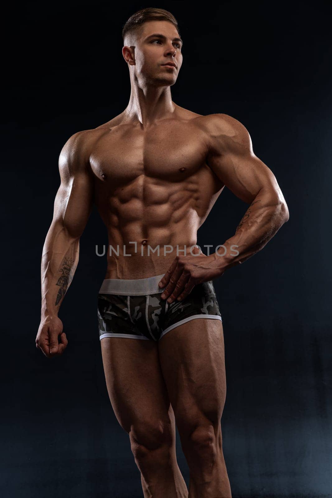 Attractive sexy bodybuilder posing in shorts in the studio on black background, demonstrating a muscular strong body. The concept of hard work in gym and body aesthetics