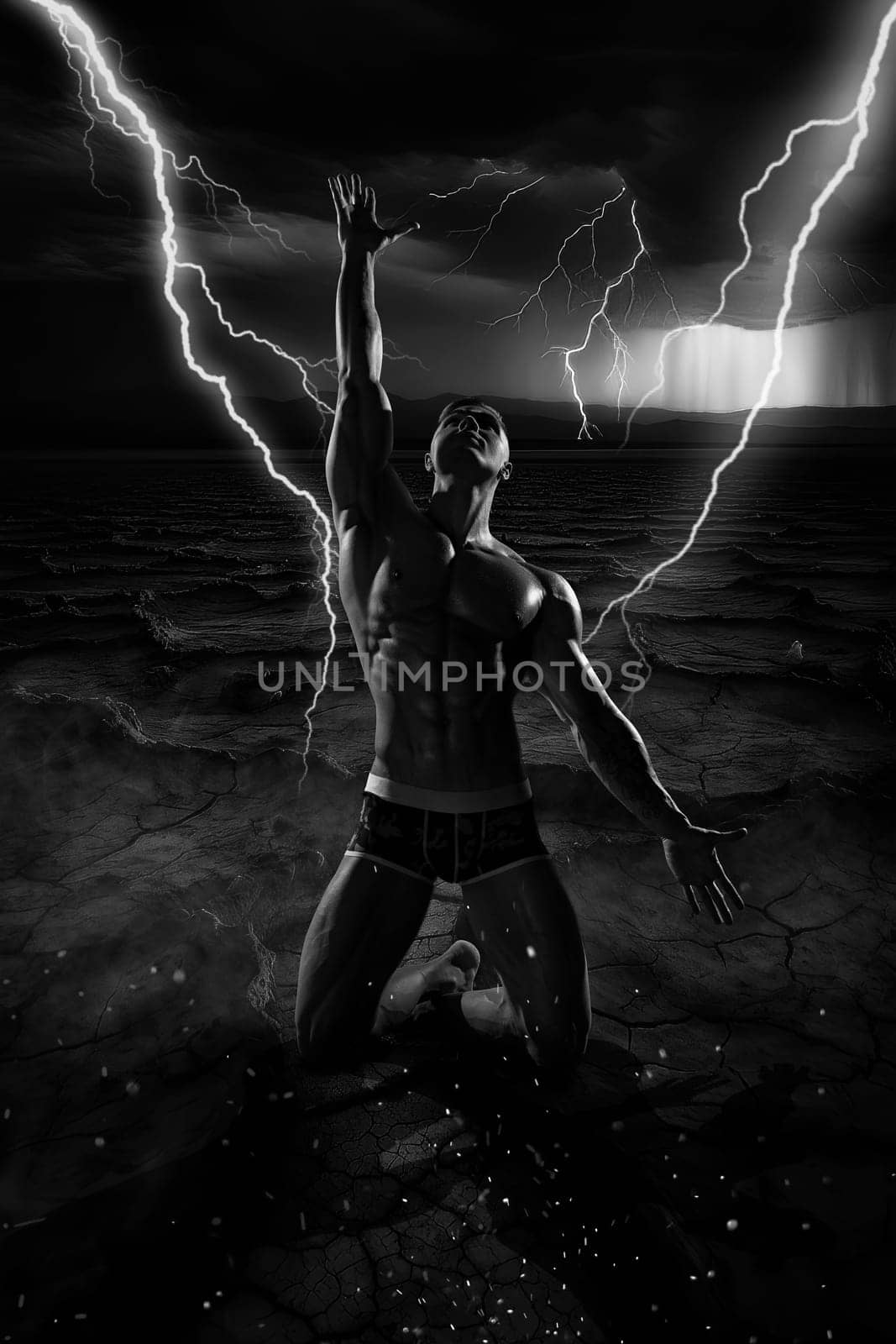 Athletic shirtless man posing kneeling on cracked dry ground with his hand outstretched towards a stormy dramatic sky with flashes of lightning
