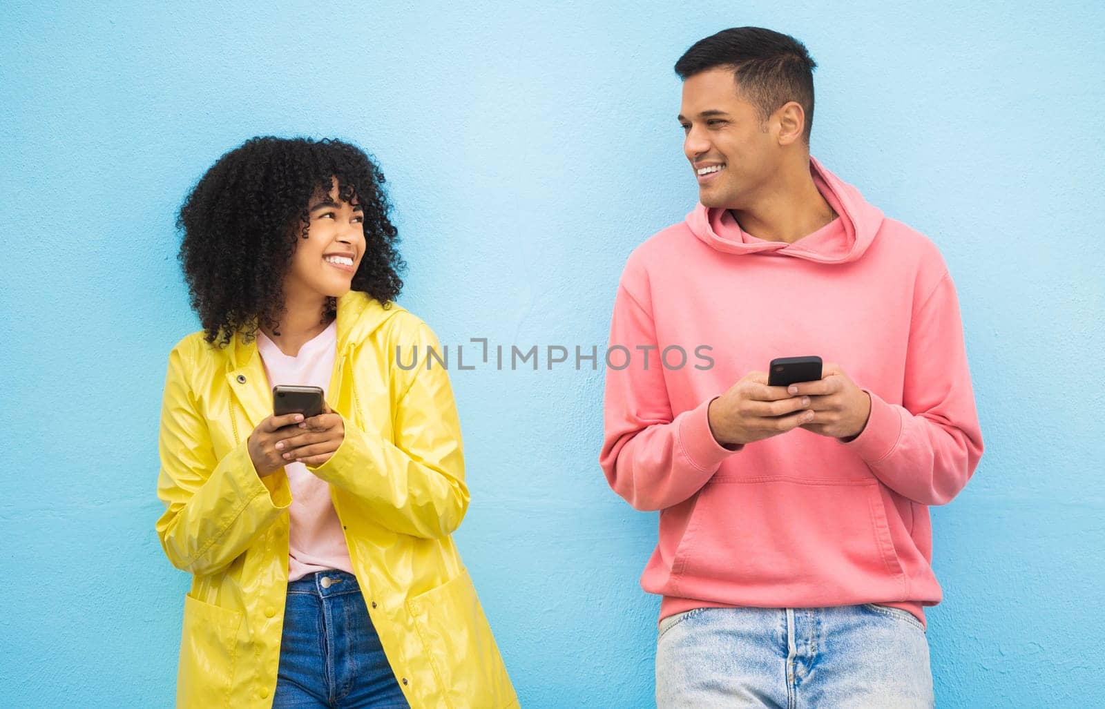 Friends, phone and smile for social media, conversation or communication against a blue studio background. Happy man and woman smiling for networking, 5G connection or chatting on mobile smartphone.