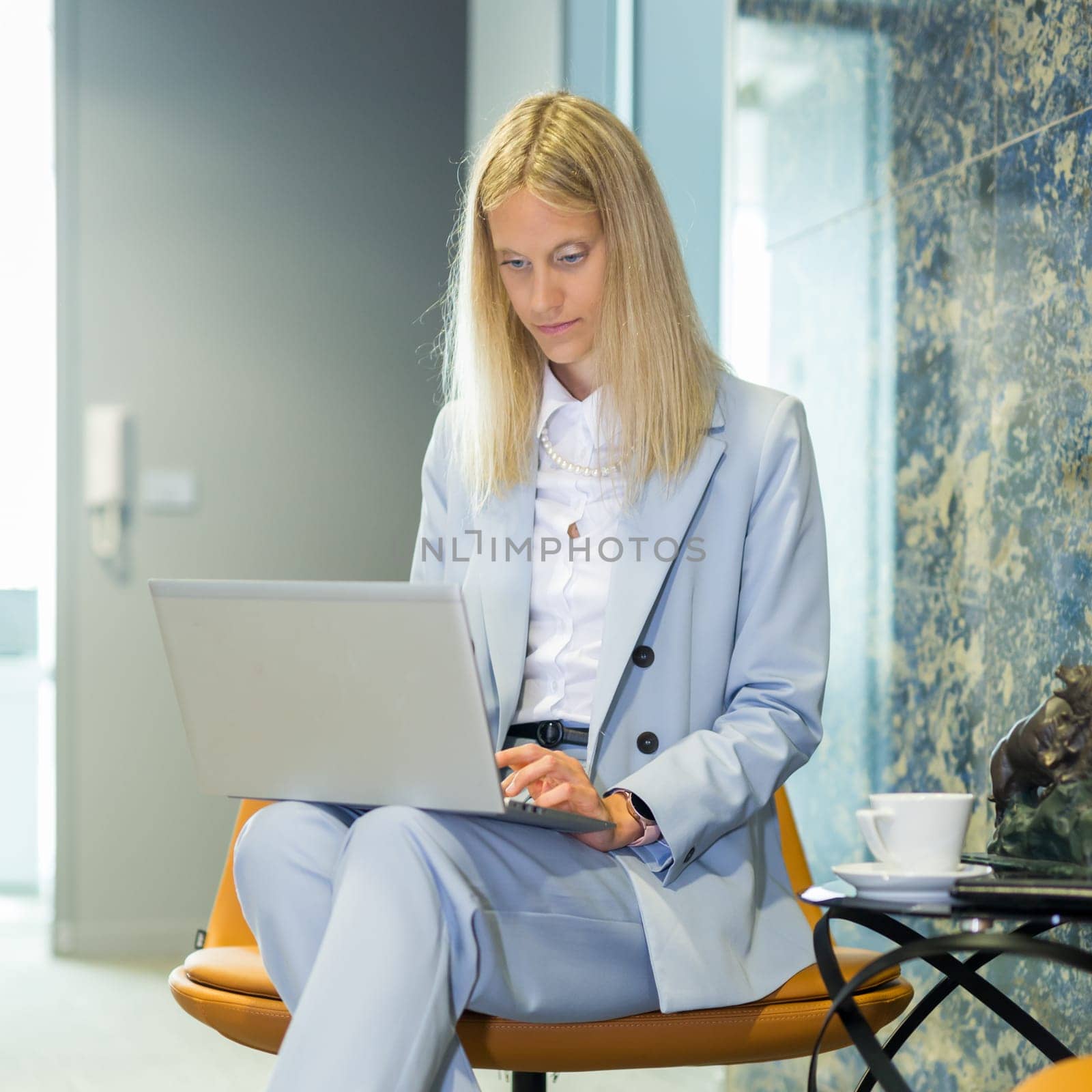 Beautiful business woman sitting at the table working on a laptop. Stylish woman in the modern office environment. by kasto