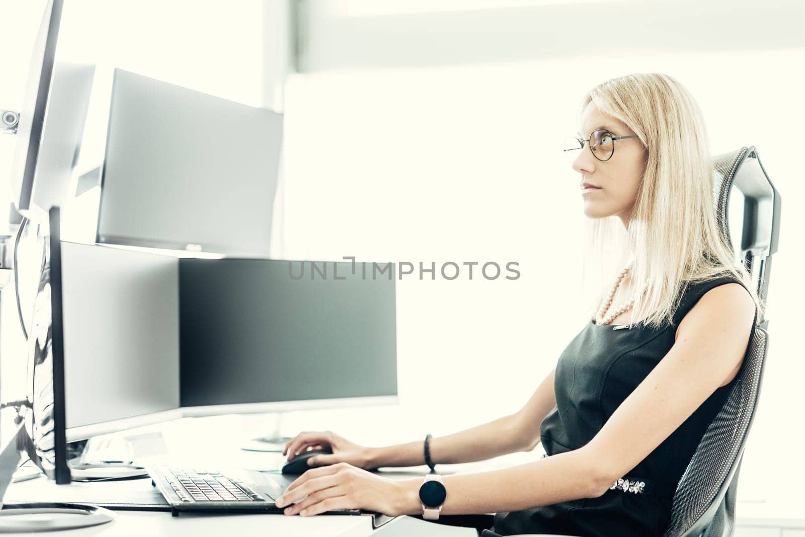 Female financial assets manager, trading online, watching charts and data analyses on multiple computer screens. Modern corporate business woman concept.