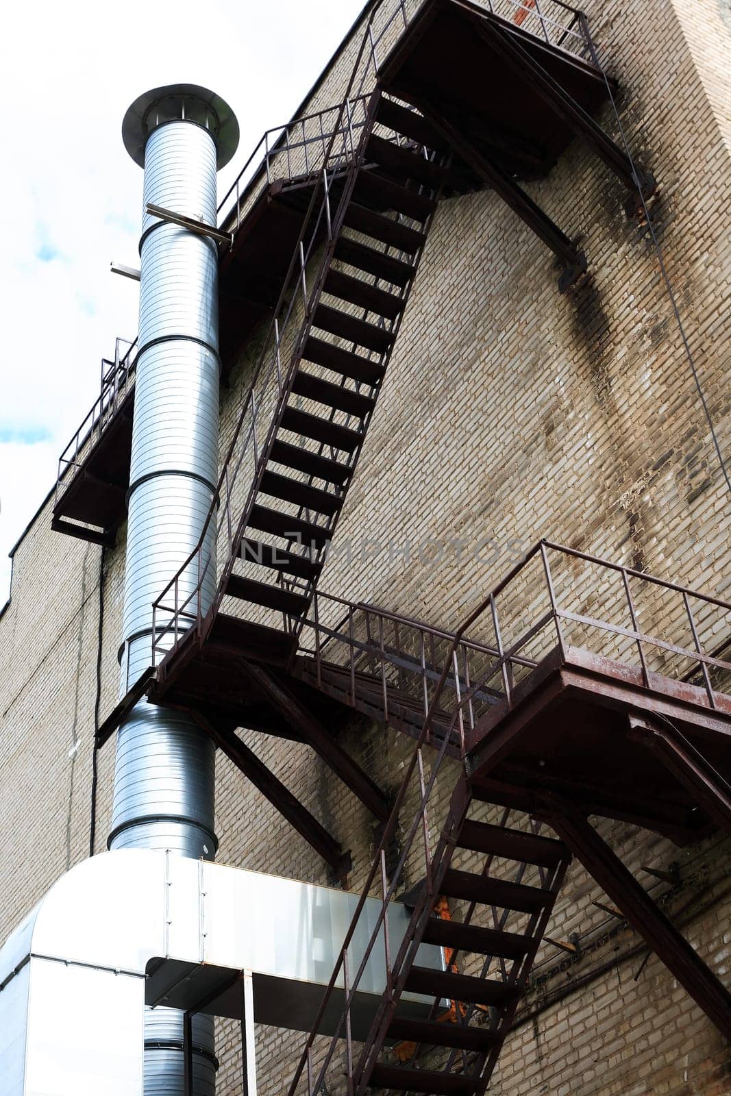 Brick wall of old factory with fire escape and metal chimney