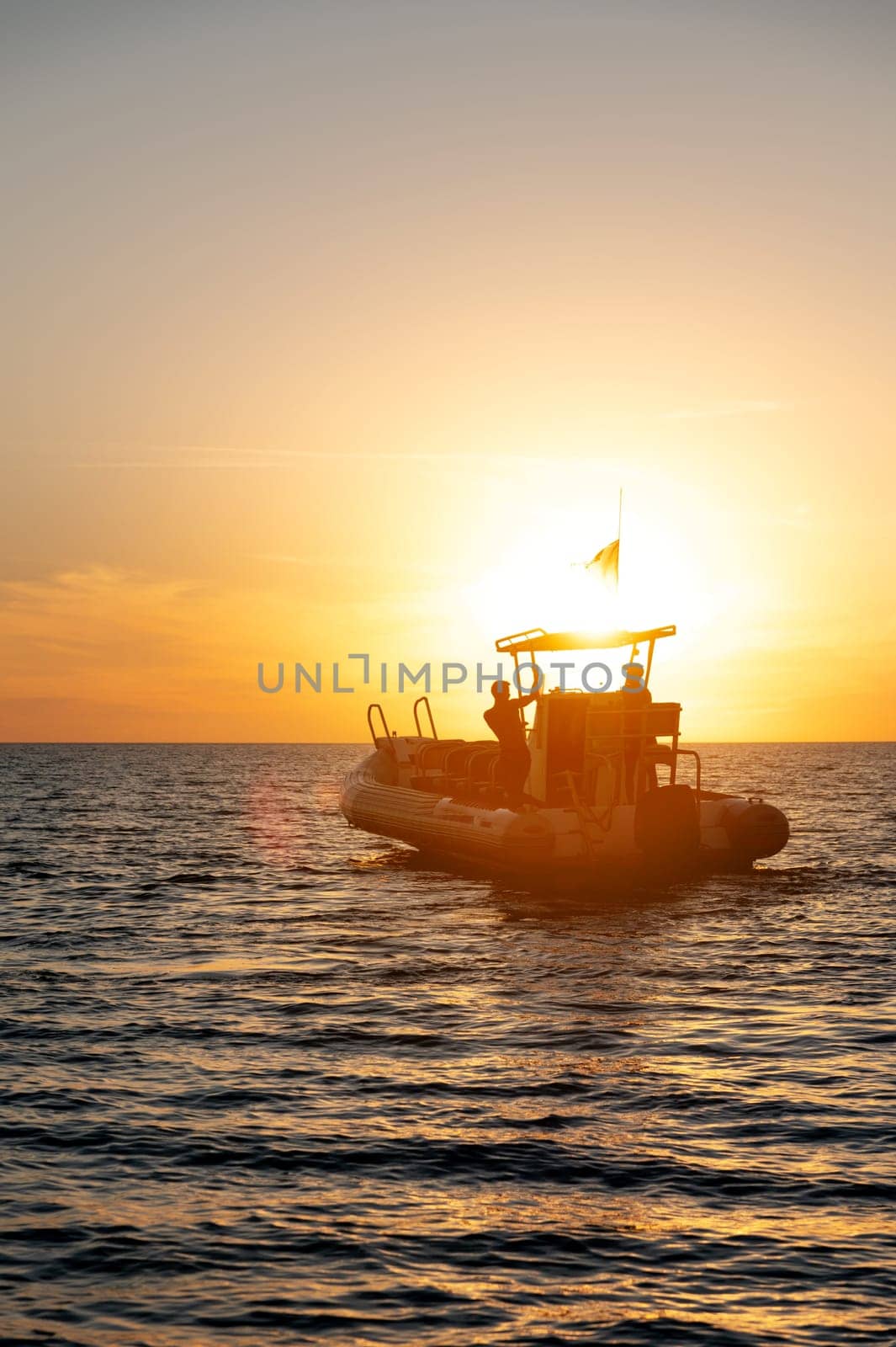 Small fishing boat with two fishermen on board in silhouette light at sunset. Seascape at sunset.