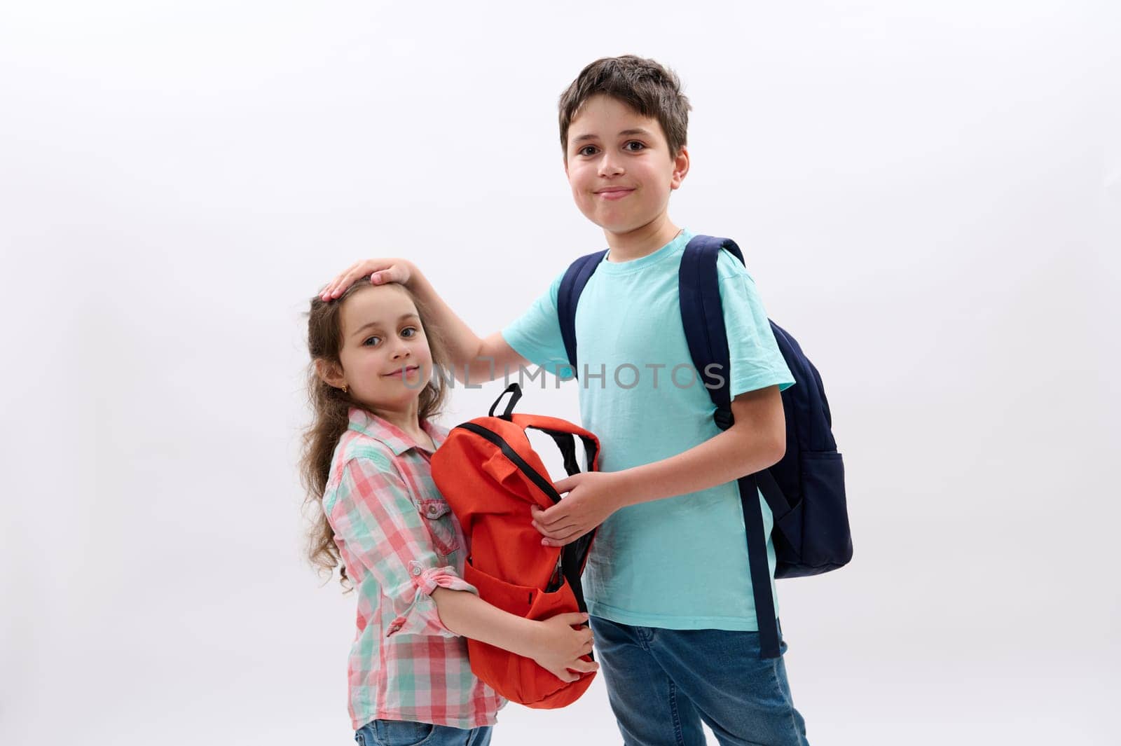 Handsome teen boy with backpack, strokes his younger sister, ready to go at school, start new semester of academic year by artgf