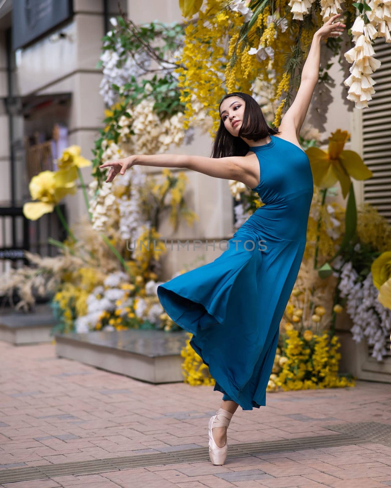 Beautiful Asian ballerina posing against the backdrop of a building decorated with flowers