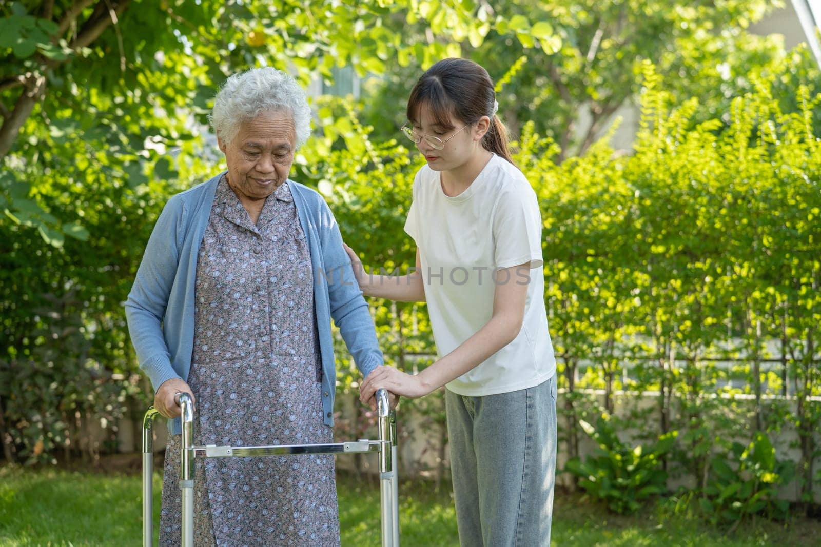 Caregiver help Asian elderly woman patient walk with walker in park, healthy strong medical concept.