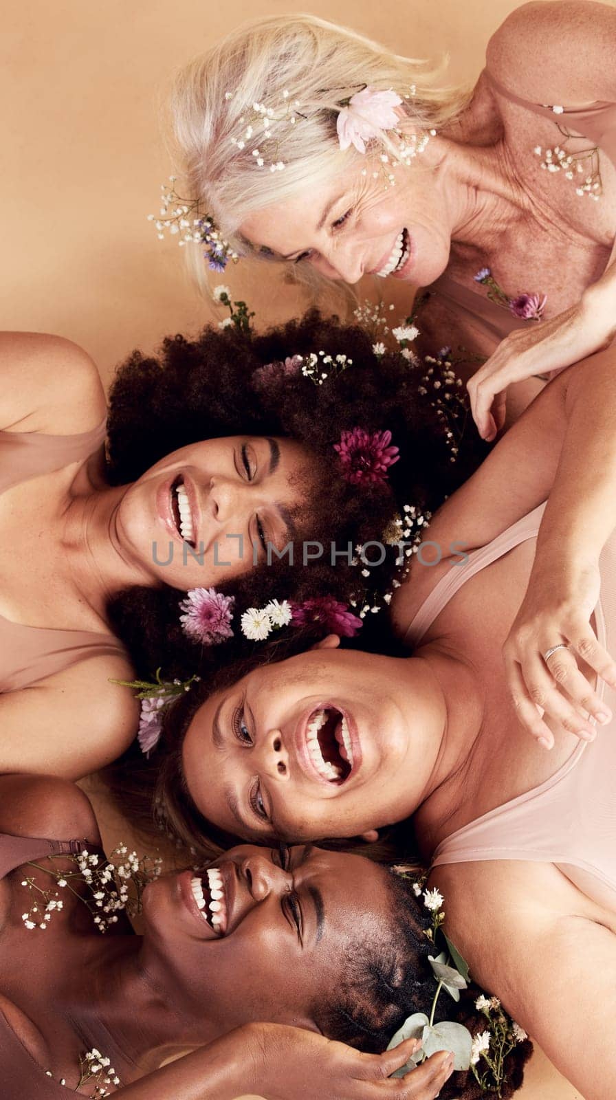 Top view, diversity and women with flowers, cosmetics and skincare on a brown studio background. Multiracial, females and ladies with body positivity, natural beauty or makeup for confidence or smile by YuriArcurs