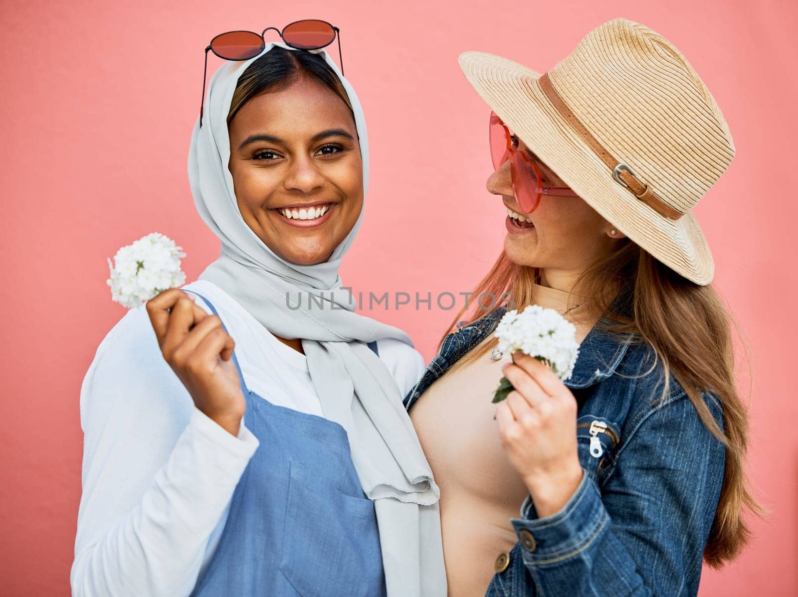 Happy, portrait and lesbian couple with flowers isolated on a pink background in a studio. Smile, looking and Muslim girl with a flower, woman and happiness about plants for romance on a backdrop by YuriArcurs