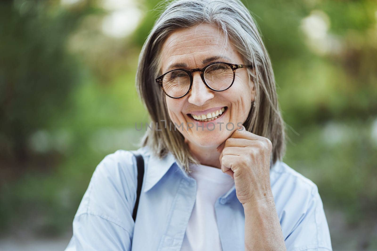 Senior woman with grey hair smiling in park. Genuine moment of happiness and joy as woman enjoys serene environment of park. Her smiling expression reflects positive outlook and contentment. . High quality photo
