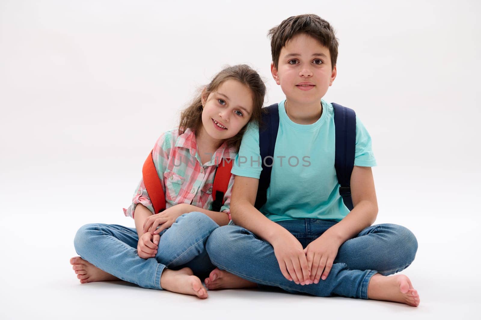 Authentic portrait of happy brother and sister, school kids with backpacks, smiling at camera, isolated white background by artgf