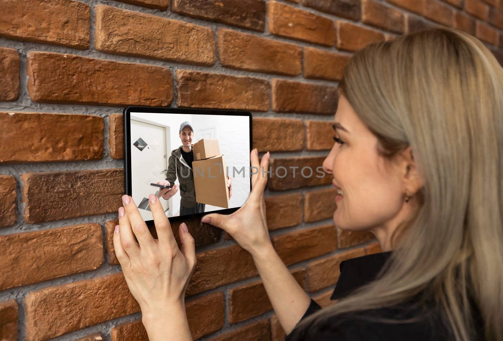 Security camera system on tablet app - Delivery man holding package in front of door cam - AI Cctv smart technology lifestyle concept by Andelov13