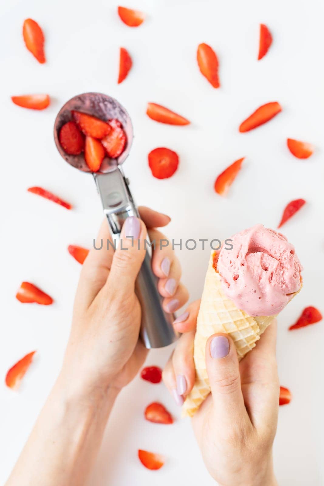 Strawberry ice cream in a cone and in an ice cream spoon on a background of fresh strawberry slices