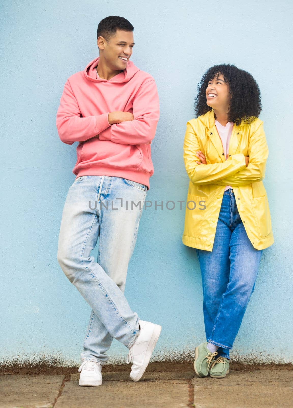 Happy couple, smile and cool fashion standing in urban town wall background for conversation, peace and relax together. Casual man, trendy woman and happiness speaking for millennial street style.