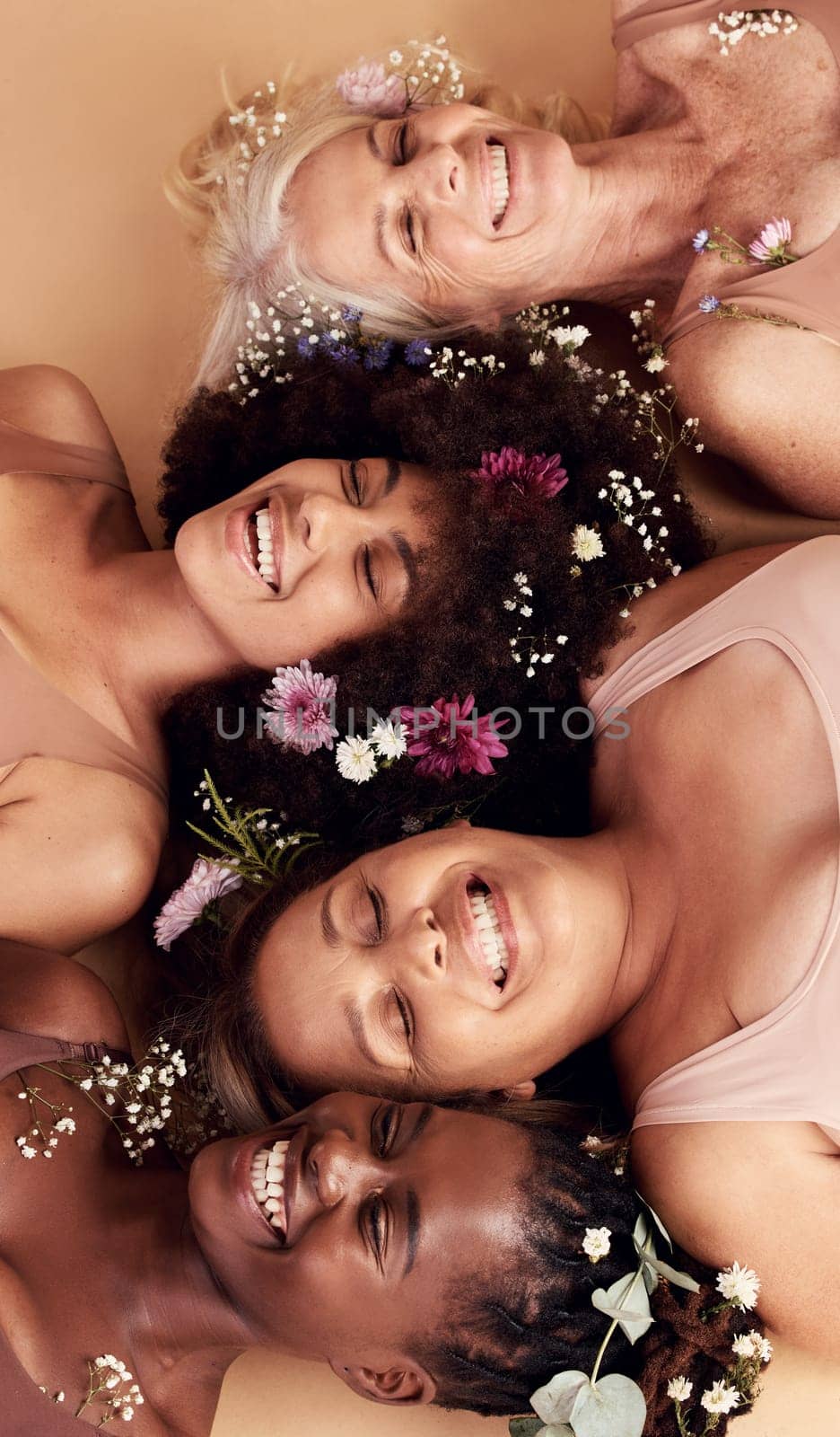 Top view, women diversity or faces with flowers on studio background in empowerment, divine feminine energy or self love. Smile, happy or skincare beauty models with plants, leaf or organic spa glow.