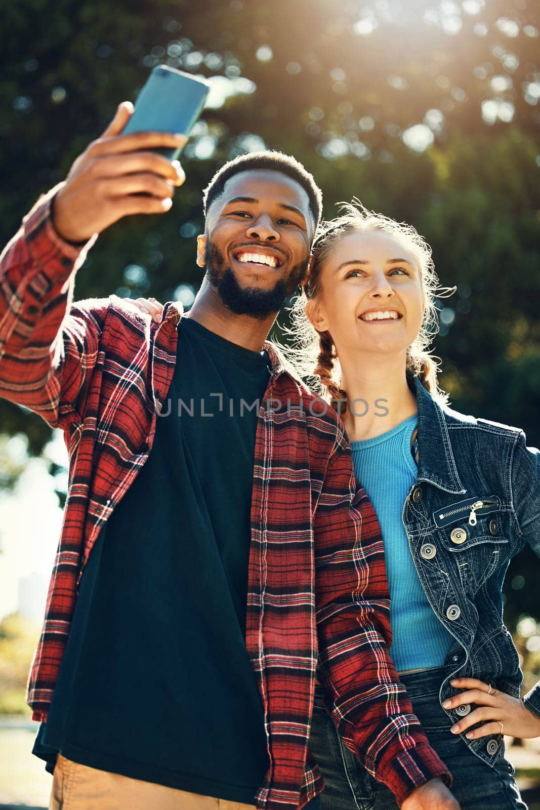 Selfie, love and happy couple on an outdoor date for their anniversary or romance together. Happiness, smile and interracial man and woman taking picture on a phone while on a walk in park in nature