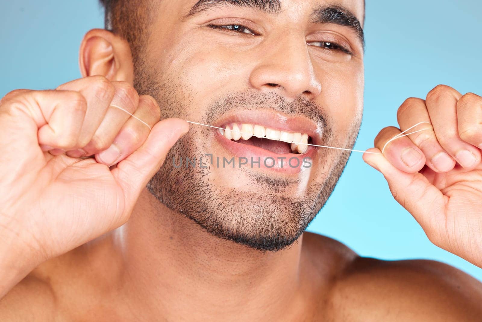 Face, dental and man floss teeth in studio isolated on blue background. Veneers, invisalign and male model from Brazil flossing, cleaning for wellness or mouth hygiene, oral care and tooth health