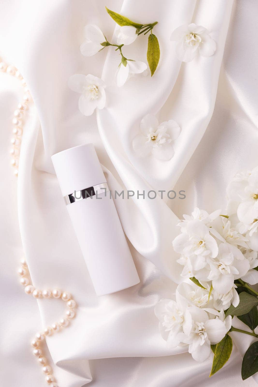 A jar of liquid cream with flowers on a white flowing satin.
