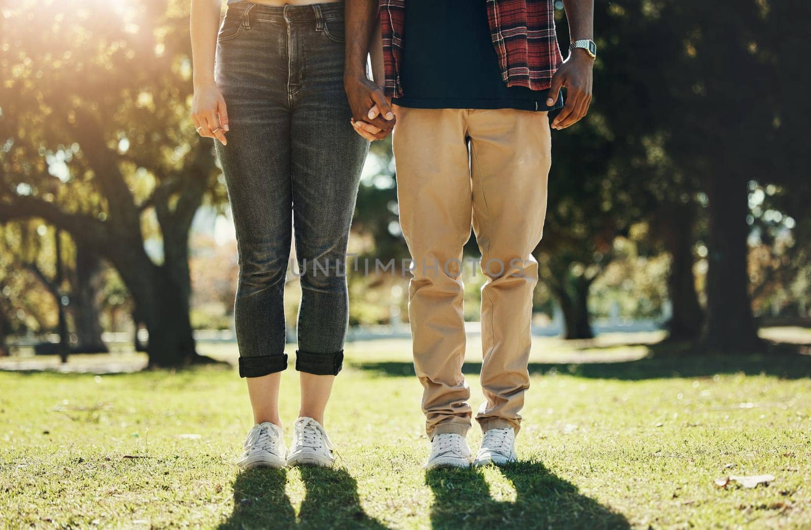 Love, holding hands and shoes of interracial couple in park for calm, freedom or support. Relax, happy and peace with feet of black man and woman standing in grass field for nature, spring or bonding.