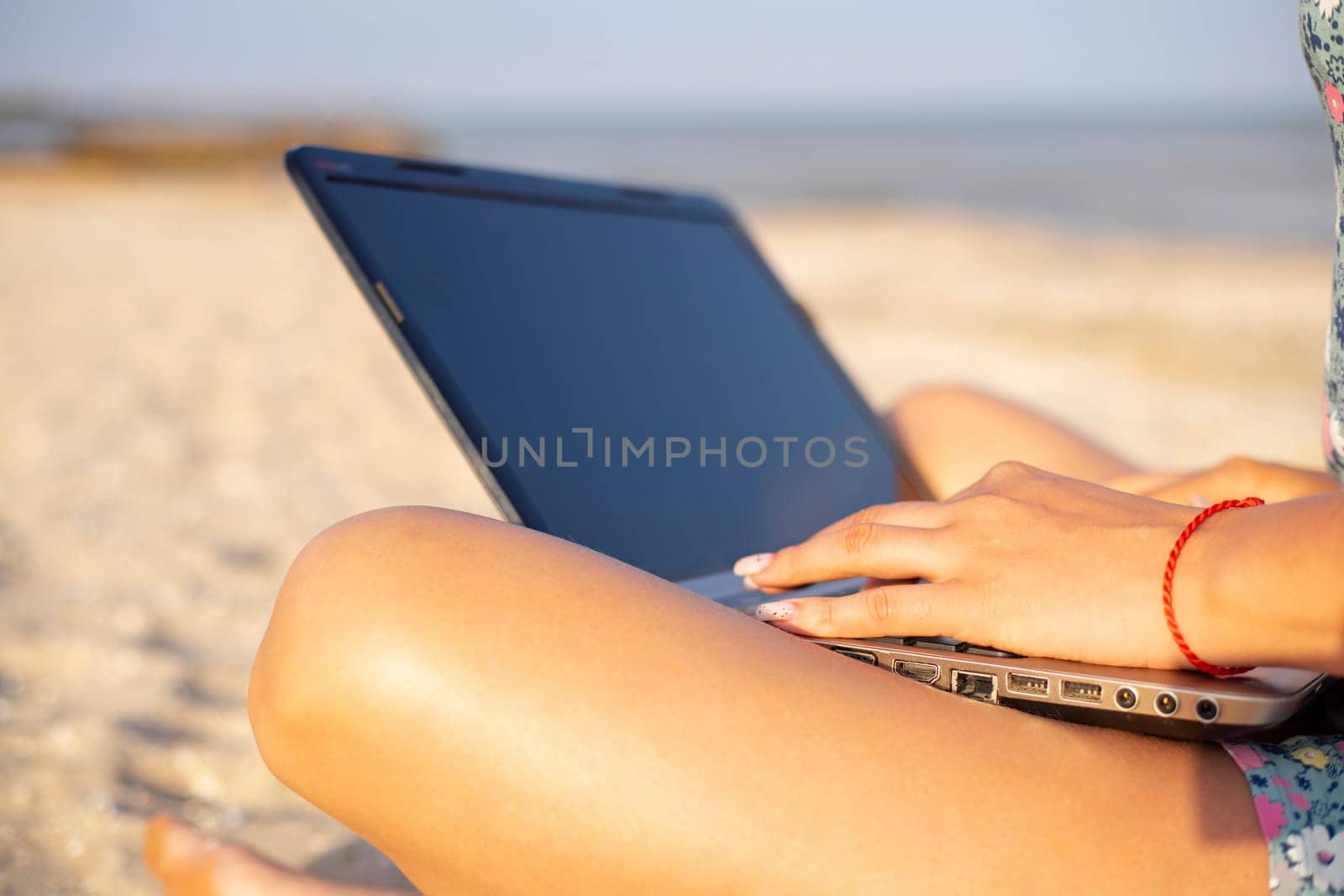 Young woman working on her laptop on the beach during sunset. by andreyz