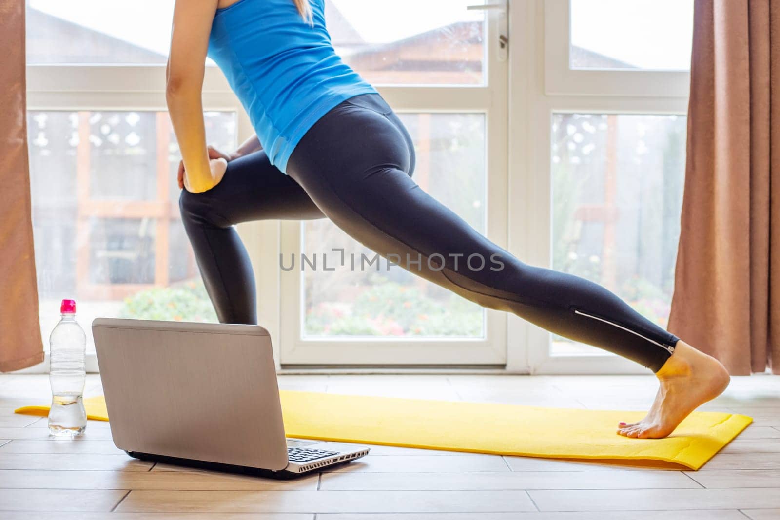 Beautiful young woman in sportswear doing sport exercises on yoga mat at home. Fitness training online with a laptop. Healthy lifestyle concept.