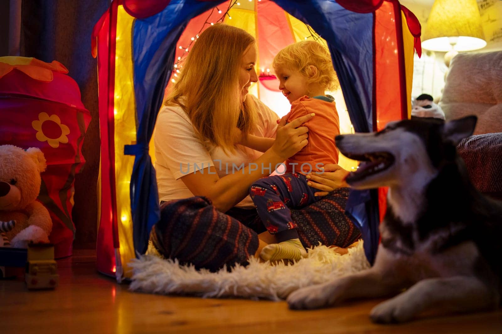 Happy loving family. Young mother and her son boy play in children room at the bedtime. Mom and lovely child are having fun with flashlights indoors. Family concept.
