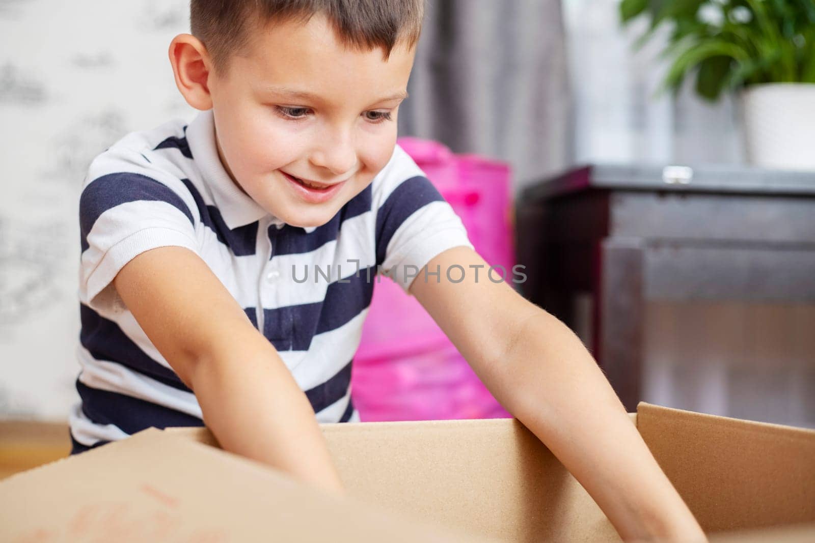 A boy is unpacking cardboard box ( gift box or parcel) at home. by andreyz