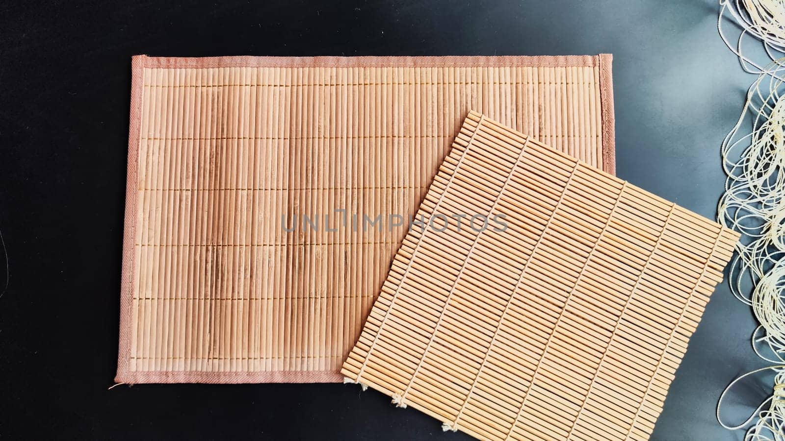 Big rectangular and small square Asian bamboo mats and napkins from yellow bamboo on black surface. Background, texture, frame, copy space, location for the photo shoot