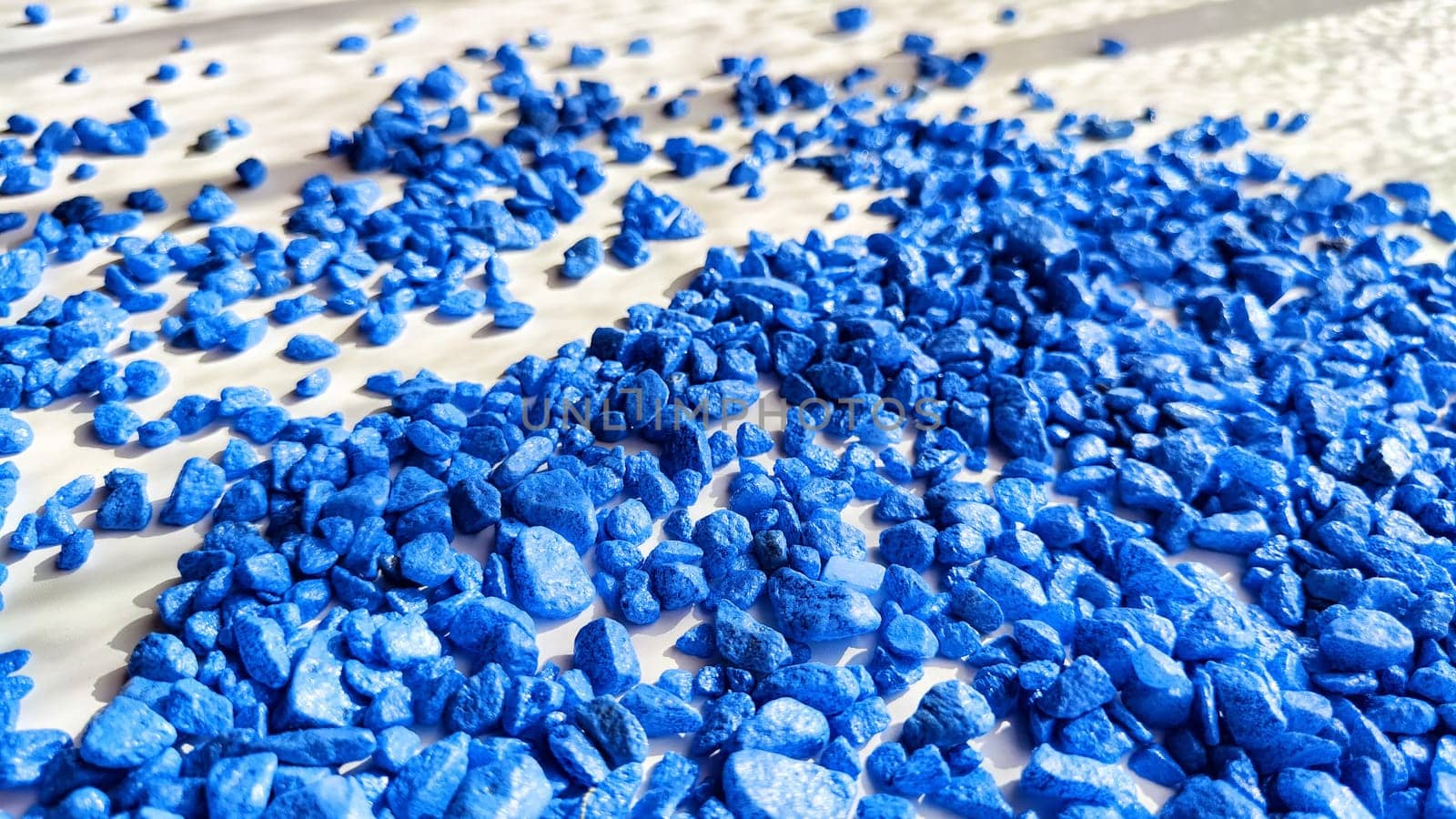 Blue painted small pebble on the surface of table under sunlight. Abstract background, texture, frame, and copy space. Supplies for crafting and handmade.