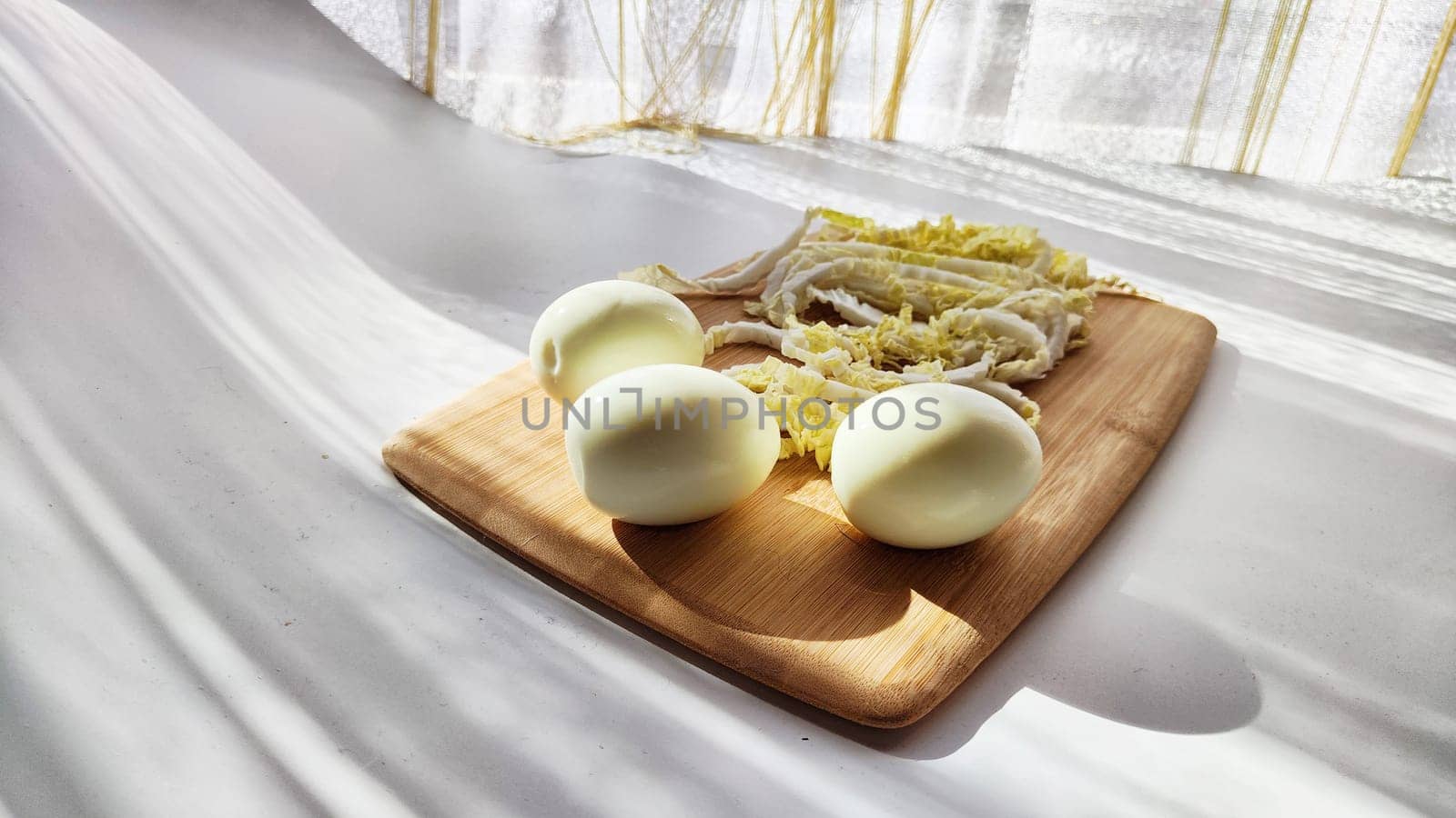 Chopped Peking cabbage and peeled eggs on cutting board as background. Cooking a healthy eco-friendly salad from natural products. Copy space and place for text