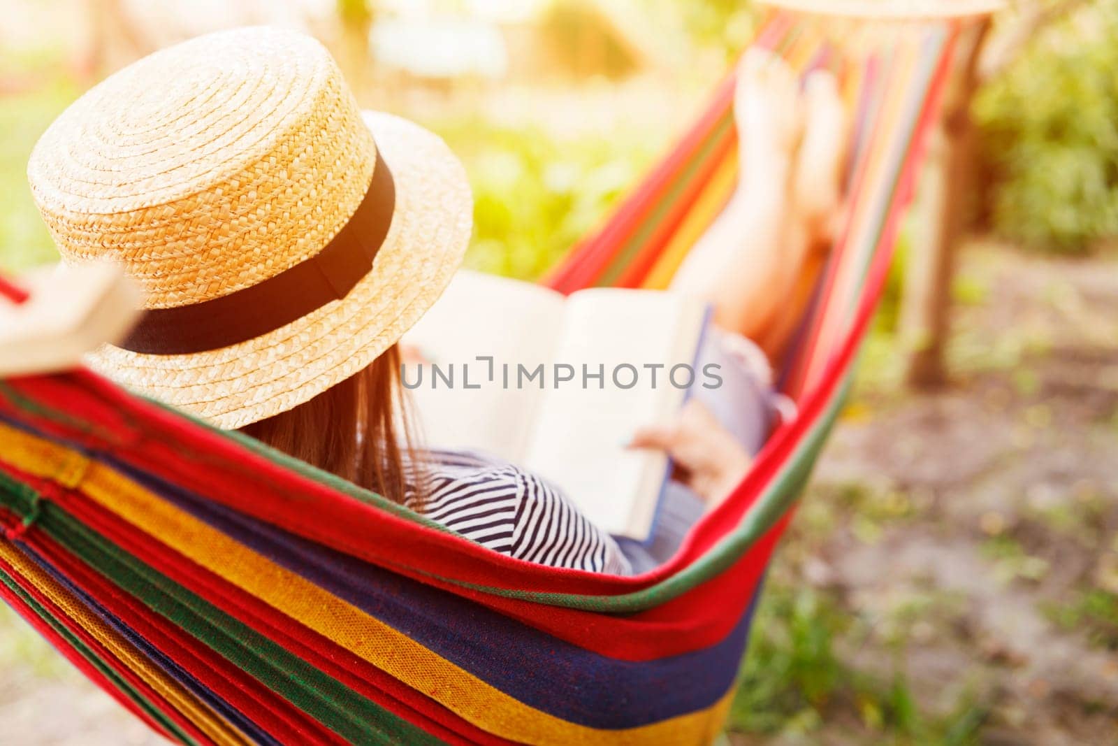 Young woman reading book while lying in comfortable hammock at green garden by andreyz