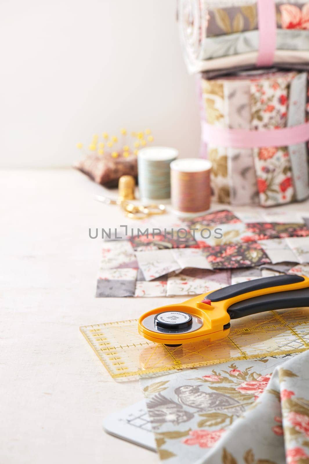 Patchwork blocks, rolls of fabric, sewing accessories on white surface
