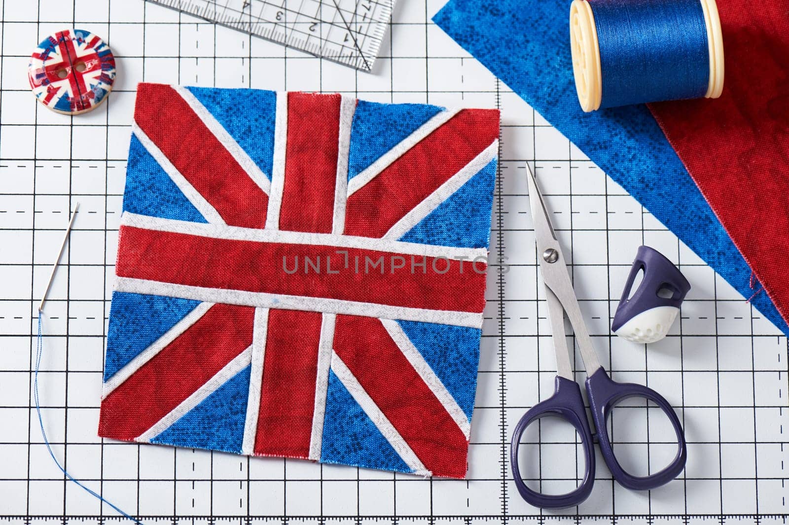 Stitched top of pincushion like Union Jack on white craft mat, sewing accessories